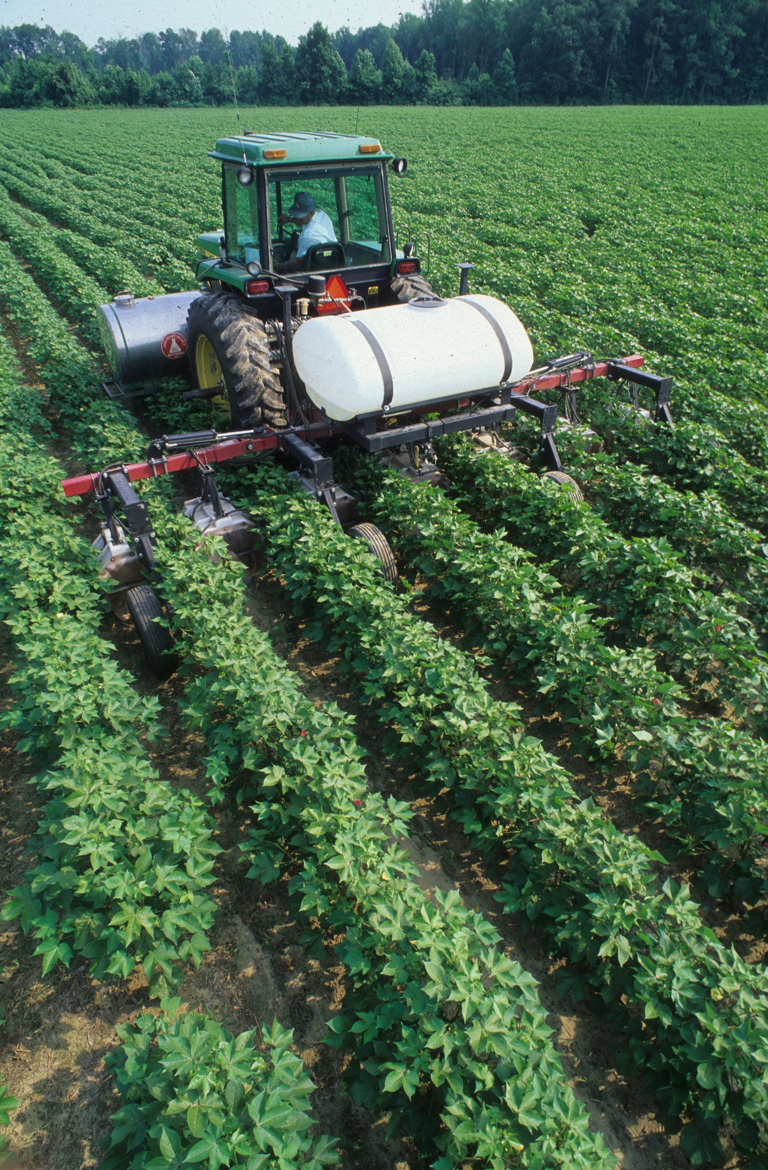 Tractor operator spraying field crops with pesticide